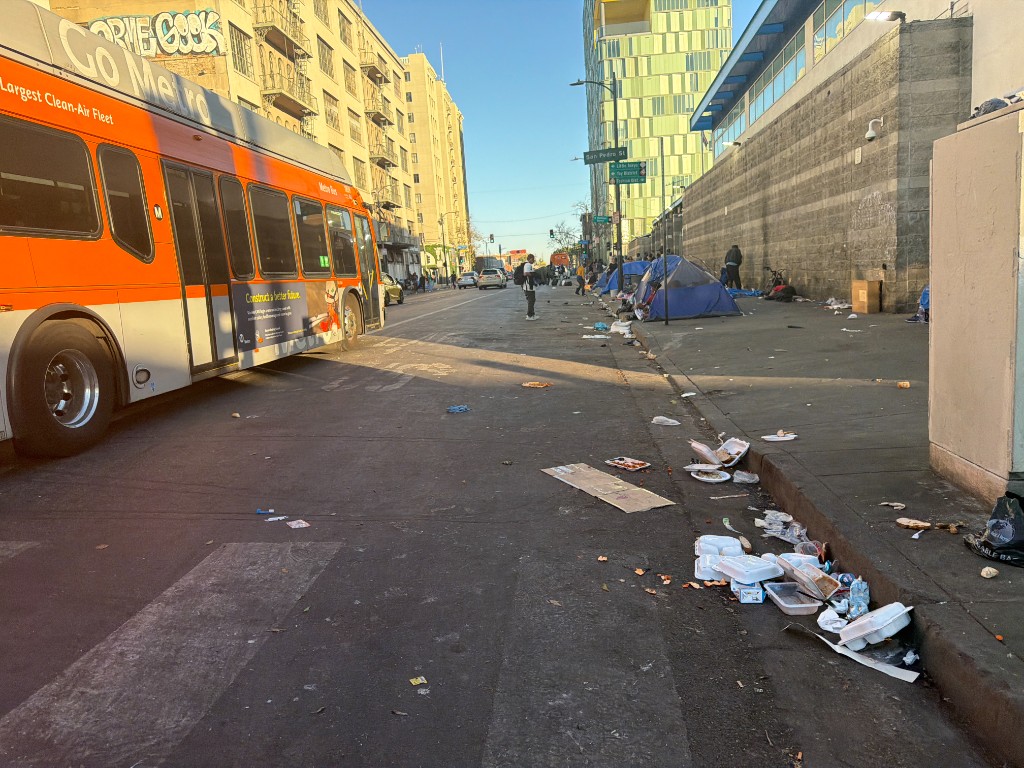 Debris litters the sidewalk along a downtown Los Angeles street as a Metro bus passes through Skid Row.