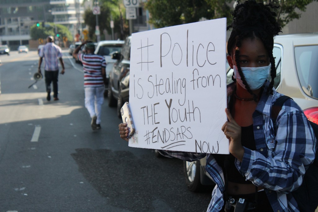 A demonstrator holds a sign reading "#Police is Stealing from THE Youth #ENDSARS NOW" during a Los Angeles End SARS rally.